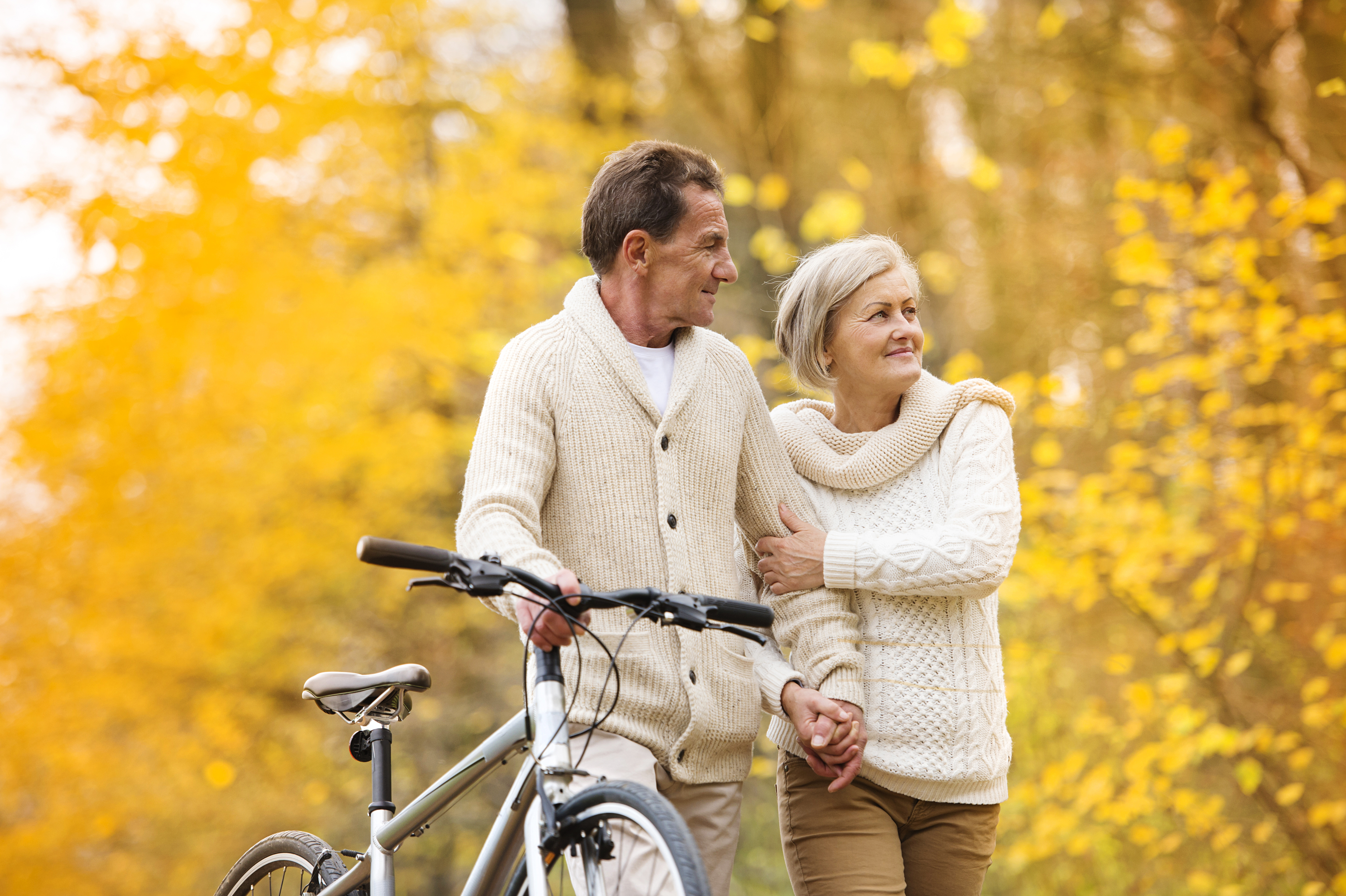 Elderly couple walking through a fall forest with a bicycle.